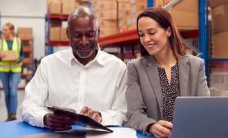Two colleagues smiling over tablet in a warehouse